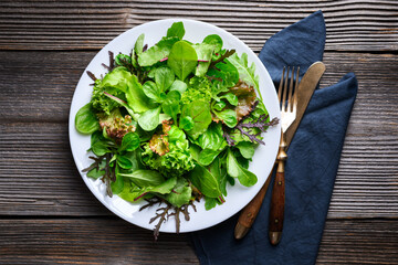 Top view of fresh salad greens mix on rustic wooden table. Food photography