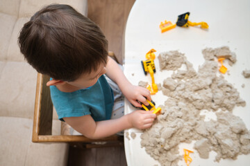 The baby boy enjoys building small constructions with kinetic sand during indoor activities. Kid aged three year