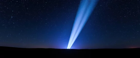 Piercing beam of light illuminates a star-studded night sky above a dark landscape, celestial,  dark night © Patthama