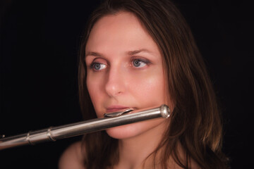 Close-up portrait of a woman playing the flute against a black background. Studio musician photography. Classical music and performance concept.