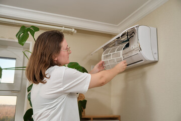 Cleaning air conditioner filter. Woman removing dust filter from wall-mounted split air...