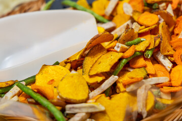 Mix of dried vegetable chips including sweet potato carrot green beans and taro with a white scoop used for light snacking healthy eating