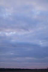 Dramatic overcast sky with layered clouds and subtle pastel hues at dusk over a distant rural landscape