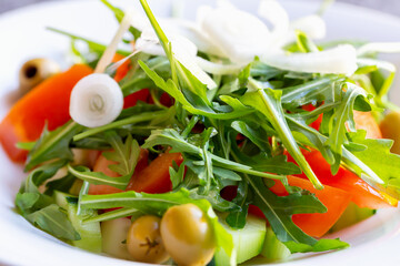 Fresh vitamin vegetable salad with arugula and olives, tomato and cucumber and white onion on a plate. Proper nutrition. Diet and health. Selective focus, defocus