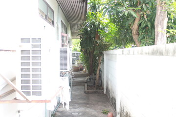 The area around the house with the air conditioner in a small garden for growing plants and large trees.