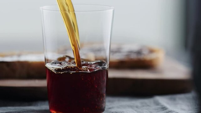 Slow motion pour cold brew coffee in tumbler glass on walnut table