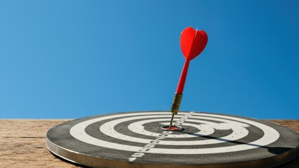Red dart hitting bullseye of target on wooden surface under blue sky, symbolizing precision and success