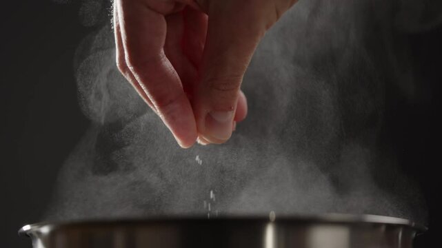 Slow motion man adding salt to boiling water in saucepan with strong backlight
