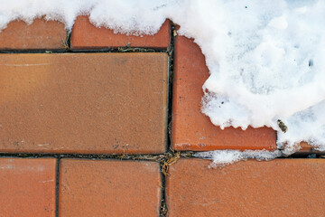 Detailed view of cracked red bricks with white snow, showing contrast between warm and cold...