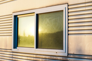 Detail of a modern sliding window on a building with a horizontally ribbed metal facade, capturing the soft light of the setting sun and subtle reflections.
