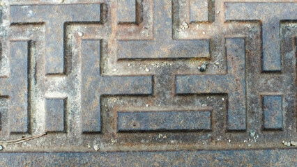 A close-up view of a metal surface with a repeating geometric pattern of raised shapes and lines, showing texture and detail.