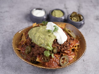 A loaded plate of beef nachos topped with melted cheese, spicy jalapeños, guacamole, sour cream, and fresh cilantro, served with extra dips