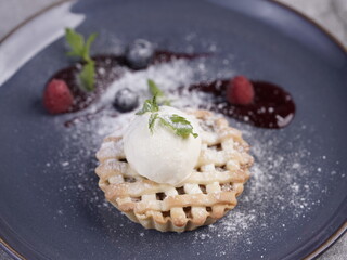 A beautifully plated mini lattice pie topped with a scoop of vanilla ice cream, garnished with powdered sugar, berry sauce, and fresh mint