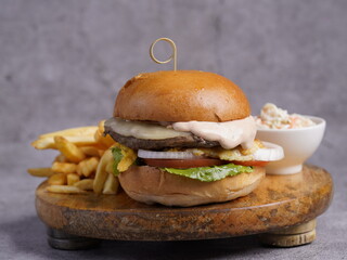A gourmet cheeseburger with melted cheese, fresh lettuce, tomato, onion, and sauce, served with crispy fries and coleslaw on a rustic wooden board