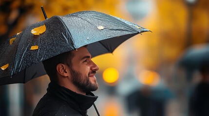 Man is smiling under an umbrella on a rainy day. The umbrella is black and has a yellow leaf on it. The man is wearing a black jacket and he is enjoying the rain