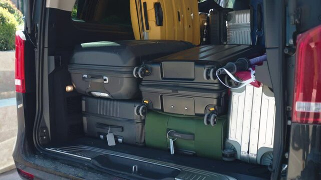 Open van trunk being unloaded with baggage on parking lot near, people putting different suitcases inside the trunk, preparation for departure, concept of business trip, family vacation, friends