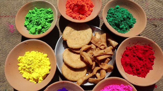 Holi festival setup with vibrant colors in clay bowls and a plate of mathri, a traditional festive snack, symbolizing the joy and culture of Holi celebrations