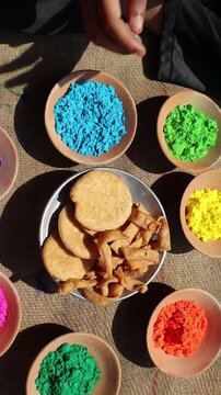 Holi festival setup with vibrant colors in clay bowls and a plate of mathri, a traditional festive snack, symbolizing the joy and culture of Holi celebrations