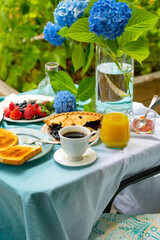 A delicious outdoor breakfast with coffee, toast with jam, fresh berries, and orange juice on a beautifully set garden table. A cozy morning with nature, flowers, and a peaceful atmosphere