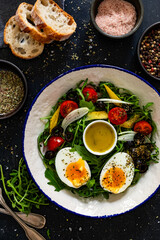 Fresh green salad with vegetables, boiled eggs and vinaigrette sauce on black table	