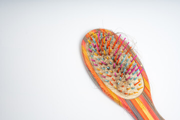 Colorful hairbrush with loose hair strands tangled in bristles on isolated white background. Close up of wooden brush filled with shedding. Grooming, care, maintenance and problem concept, top view