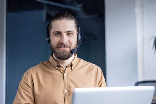 A friendly customer service representative wearing a headset smiles while working at his computer, ready to assist customers with their inquiries. - Powered by Adobe