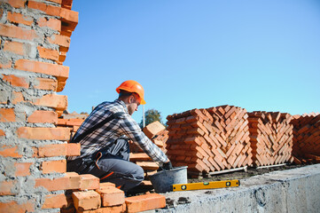 Bricklayer industrial worker installing brick masonry on exterior wall with trowel putty knife
