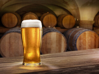 Glass of chilled beer on old wooden table and wooden beer casks at the background.