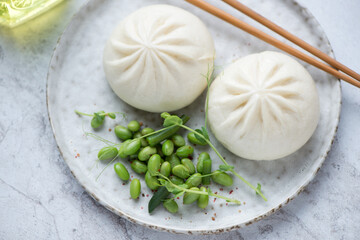 Freshly cooked chinese baozi with edamame beans on a grey plate, horizontal shot, middle closeup