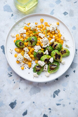White plate with corn, grilled Brussels sprouts and cheese, vertical shot on a white and blue granite background, high angle view with space