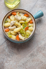 Turquoise serving bowl with chicken gnocchi soup on a brown granite background, vertical shot with space, high angle view