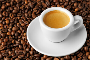 Small white espresso cup brimming with fresh, aromatic coffee resting on bed of roasted beans, creating an inviting and visually striking scene
