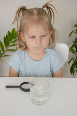 Child examines and examines water under a magnifying glass. Selective focus