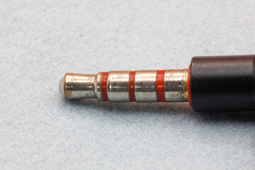 Detailed shot of a headphone plug tip, showing metal segments and red insulators on a fabric...