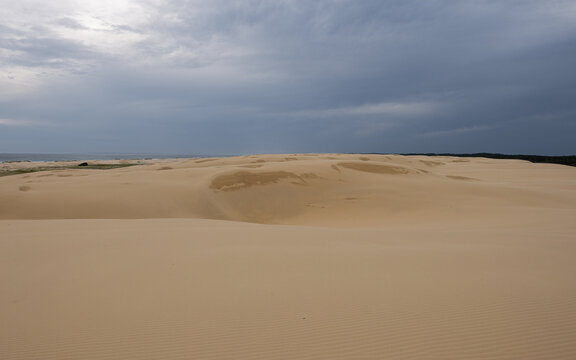 Empty sand dune with cloudy overcast sky.