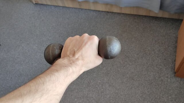 Man holds a dumbbell in his hand at home. Man exercises at home. First person view