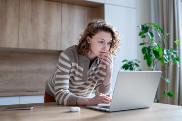 Focused woman freelancer engaged in remote work, thoughtfully analyzing data on laptop from home. Concentrated female carefully looks at screen computer, reflecting on solutions, brainstorming ideas.