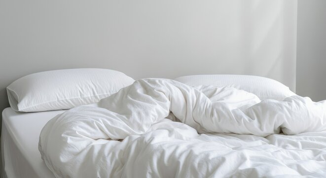 Unmade bed with white sheets and pillows in natural light