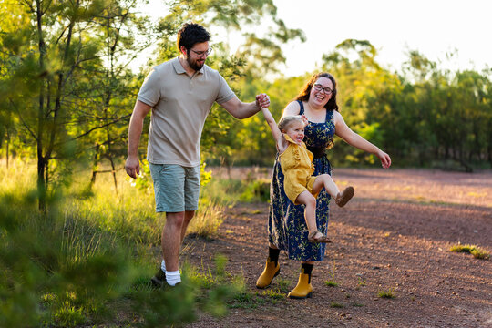 Happy young Australian family parents swinging toddler kid together in countryside