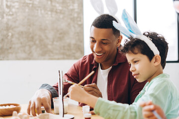 Dad and child painting easter eggs at home, wearing bunny ears