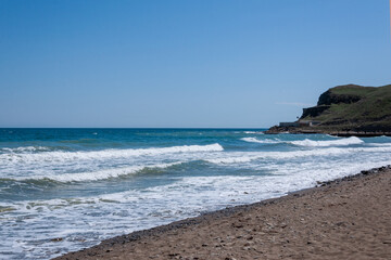 View of coastline with blue sea and waves crashing against rockshelf.