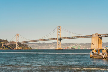 The Bay Bridge spans the waters of San Francisco Bay with a clear blue sky overhead.