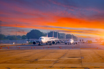 Row of airplanes at airport in parking lot in morning at dawn with red sky and clouds