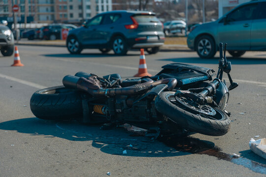 Black motorcycle with serious damage is on the asphalt. Accident close-up. Lost control and fell. Driving hazards. Collisions with another vehicle. Broken headlight and bent handlebars.