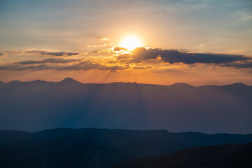 The setting sun over the mountains, the beautiful sun's rays shine through the clouds, the natural background, freedom, tranquility and peace