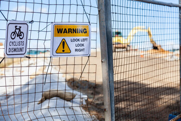 Cyclists dismount sign on fence near construction site