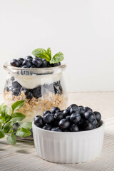 Fresh blueberry in bowl, yogurt with granola and forest blueberry and mint in glass jar Copy space