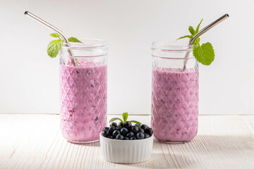 Two glasses of superfood and antioxidant blueberry smoothie with metal drinking straws on blue white