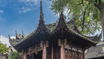 Fototapeta premium Beautiful Chinese pagoda. The roof edges are curved. Ornaments, carvings on cornices and walls. A green tree branch on a background of blue sky and clouds. China. Shanghai. Yu Garden. Yuyuan