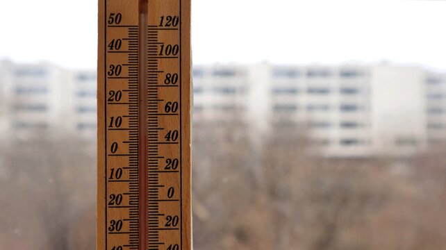 Wooden thermometer near a window. A close-up of a wooden thermometer measuring the temperature near a window with an urban landscape in the background.
